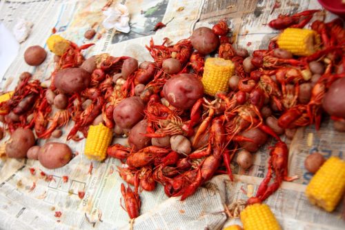A messy spread of boiled crawfish, potatoes, and corn on a table covered with newspaper.