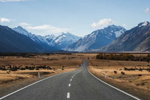 A winding road stretches through a vast valley, flanked by mountains and a clear blue sky.
