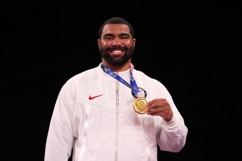 A smiling athlete in a white jacket holds a gold medal, celebrating a victory.