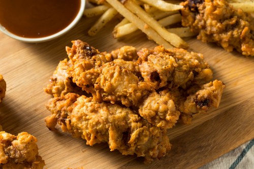 A wooden platter with crispy fried chicken pieces and French fries, accompanied by a small bowl of dipping sauce.