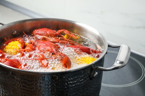 A pot of boiling water with red lobsters and corn on the cob, bubbling on a stovetop.