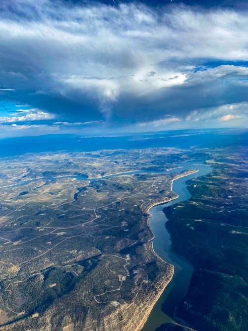 Aerial view of a winding river surrounded by green hills and blue skies with scattered clouds.