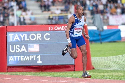 An athlete in a blue and white uniform runs on a track, with a scoreboard displaying "TAYLOR C USA ATTEMPT 1" in the background.