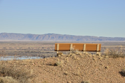 A wooden bench on a rocky outcrop overlooking a vast landscape with mountains in the distance and a calm body of water.
