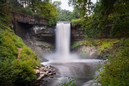 A serene waterfall cascades over rocky cliffs, surrounded by lush greenery and a tranquil pool below.