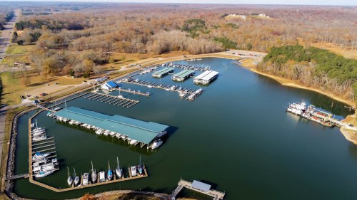Aerial view of a marina with boats docked, surrounded by trees and a calm water body in autumn colors.