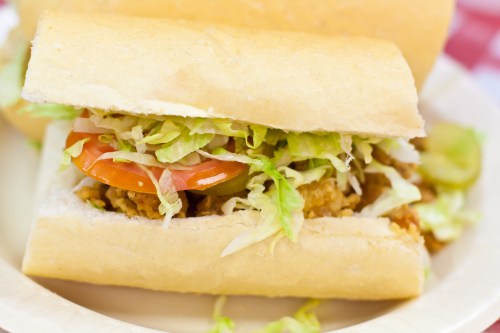 A close-up of a sandwich filled with lettuce, tomato, and crispy fried chicken in a soft bun.