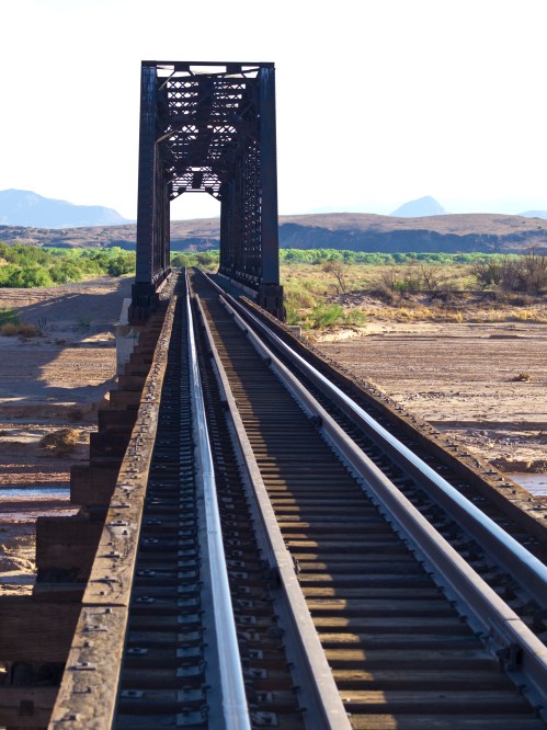 A railway bridge spans a dry landscape, with tracks leading into the distance under a clear sky.