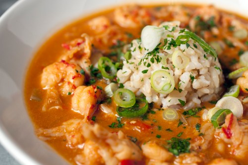 A bowl of shrimp gumbo with rice, garnished with green onions and herbs, showcasing a rich, flavorful broth.