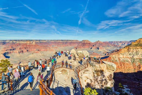 A crowded viewpoint at the Grand Canyon, showcasing vast rock formations and a clear blue sky.