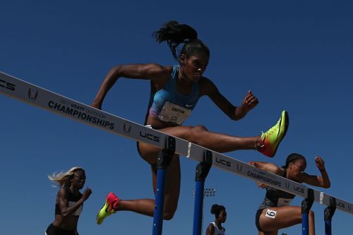 A female athlete hurdles over a barrier during a race at the 2017 USATF Outdoor Championships under a clear blue sky.