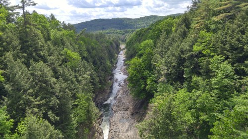 A scenic view of a river winding through a lush green forested valley under a partly cloudy sky.