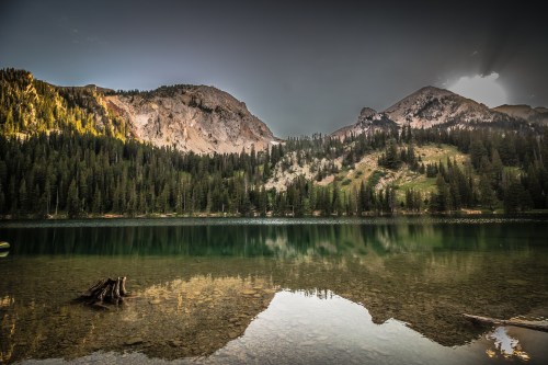 A serene lake surrounded by mountains and dense forests, reflecting the landscape in calm waters.