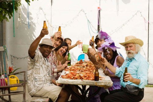 A diverse group of people celebrating around a table filled with food and drinks, smiling and raising their glasses.