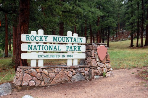 Sign for Rocky Mountain National Park, established in 1915, surrounded by trees and grassy area.
