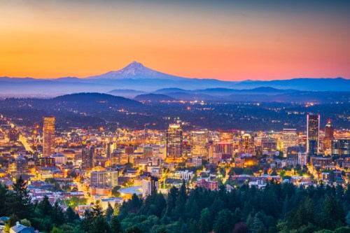 A panoramic view of Portland at sunset, with Mount Hood in the background and city lights twinkling below.