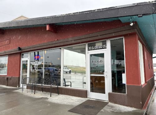 Exterior of a red restaurant building with large windows, a "TO GO" sign, and a bench outside. Rain is visible.