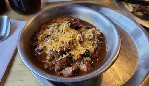 A bowl of hearty chili topped with shredded cheese, featuring chunks of meat and black beans.