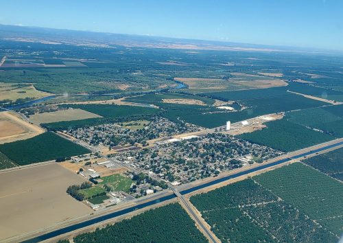 Aerial view of a small town surrounded by farmland and orchards, with a river and highway visible in the landscape.