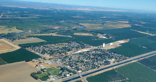 Aerial view of a rural area with fields, a small town, and a river winding through the landscape.