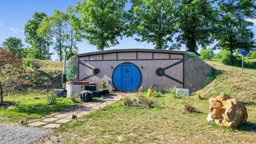 A whimsical, round house with a blue door, surrounded by greenery and a stone pathway.