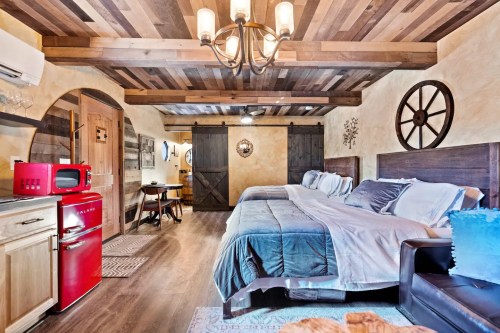Cozy bedroom with wooden beams, two beds, a vintage red fridge, and rustic decor. Warm, inviting atmosphere.