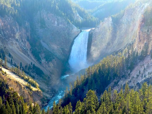 A stunning waterfall cascades down a rocky cliff, surrounded by lush green trees and mountains in the background.