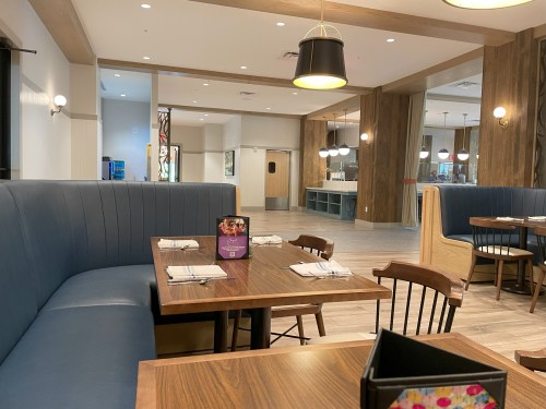 Interior of a restaurant featuring blue booths, wooden tables, and modern lighting, with a spacious and inviting atmosphere.