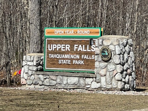Sign for Upper Falls at Tahquamenon Falls State Park, indicating it's open year-round, surrounded by trees.