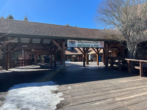 A wooden deck area with a sign for "Tahoe Tavern Falls Brewery & Pub" under a clear blue sky. Snow patches visible.