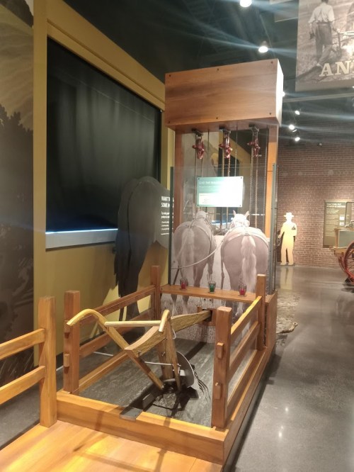 A wooden display featuring a plow and two horse silhouettes in a museum setting.