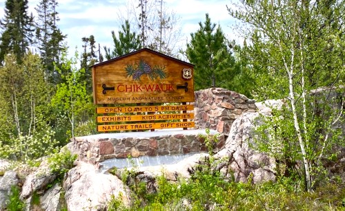Sign for Chik-Wauk Museum and Nature Center, with hours and activities listed, surrounded by trees and rocks.