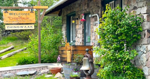 A stone building with a wooden sign reading "Welcome Chik-Wauk" and greenery in front, creating a rustic atmosphere.