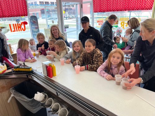 A group of children and adults sit at a counter in a diner, enjoying drinks and desserts together.