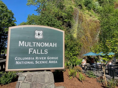 Sign for Multnomah Falls in the Columbia River Gorge National Scenic Area, surrounded by greenery and outdoor seating.