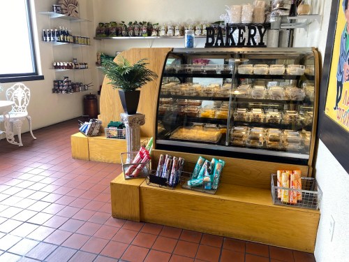 A bakery display case filled with pastries, surrounded by shelves of jars and snacks in a cozy shop interior.