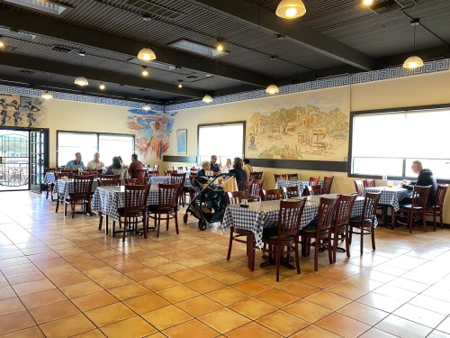 A spacious restaurant interior with checkered tablecloths, murals on the walls, and diners seated at tables.