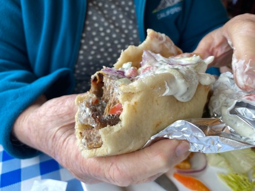 A person holds a large, stuffed wrap filled with meat, vegetables, and sauce, partially unwrapped in a casual dining setting.