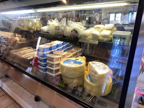 A display case filled with various types of cheese and dairy products, wrapped and organized on shelves.