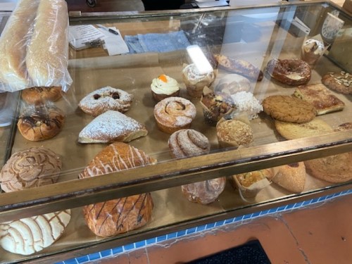 A display case filled with various baked goods, including pastries, cookies, and bread rolls.