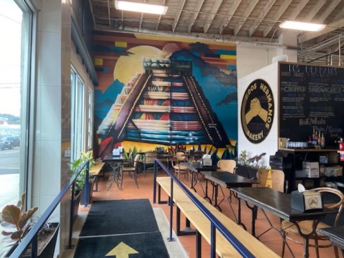 Colorful mural of a pyramid on a wall inside a bakery, with tables and chairs arranged in the foreground.