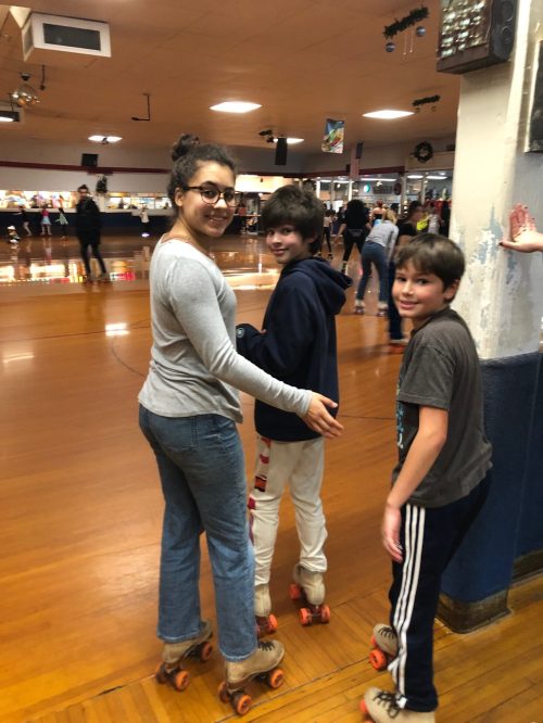 A group of three children roller skating in a rink, smiling and enjoying their time together.