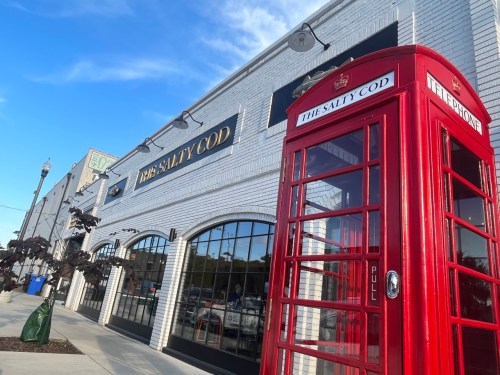 A red telephone booth stands in front of a restaurant named "The Salty Cod" with a blue sky above.