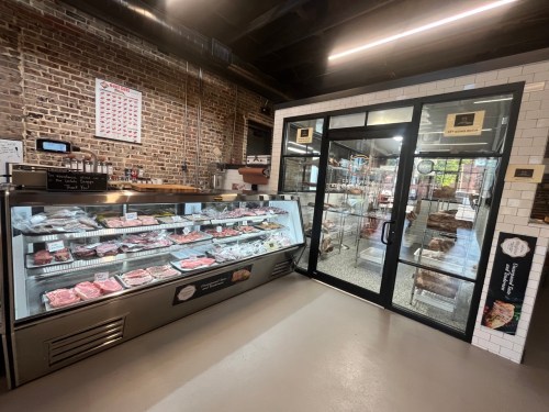 A modern butcher shop featuring a glass display case filled with various meats and a glass entrance door.