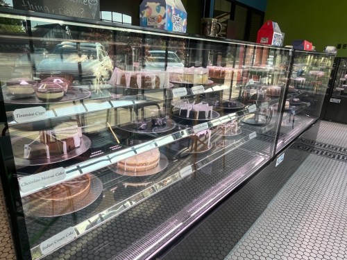 Display case filled with various cakes and desserts, including chocolate mousse and tiramisu, in a bright shop.
