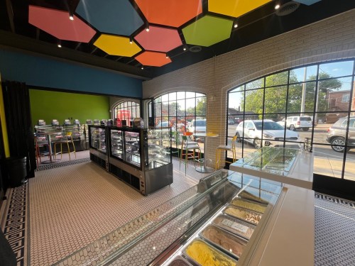 Bright ice cream shop interior with colorful hexagonal ceiling tiles, display cases, and large windows.