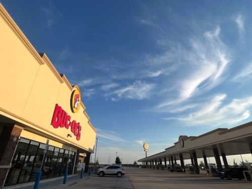 A wide shot of a Buc-ee's gas station with a clear blue sky and a few cars parked in the lot.