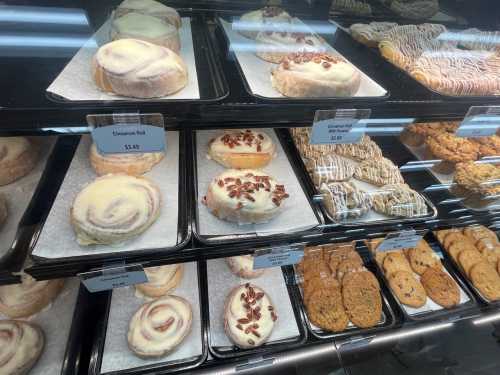 A display case filled with various pastries, including cinnamon rolls, pecan rolls, and assorted cookies.