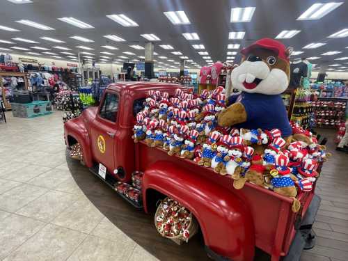 A vintage red truck filled with plush bears wearing patriotic outfits, with a large bear mascot sitting in the back.