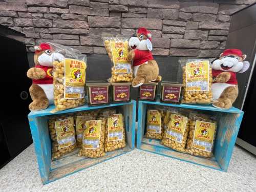 Two wooden crates display bags of snacks, with plush squirrels wearing red shirts beside them, set against a stone wall.